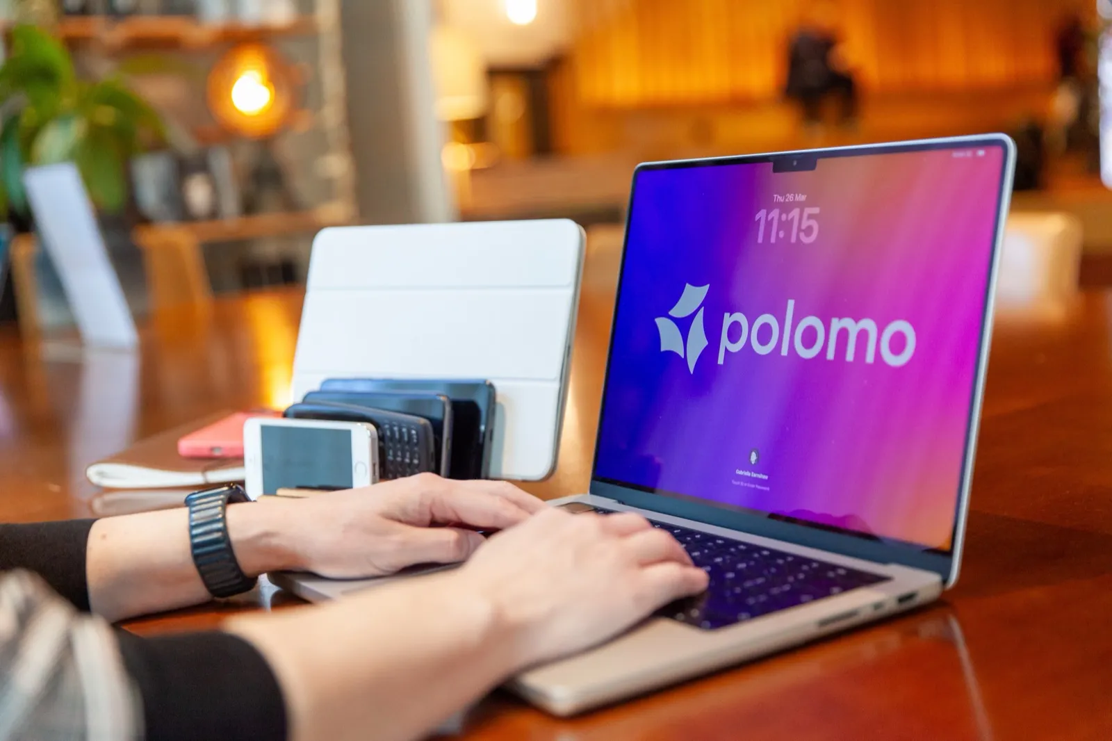 Hands typing on a laptop displaying the Polomo brand screen, with mobile devices arranged nearby